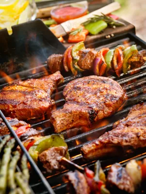 Paula Deen Southern bourbon-glazed pork chops grilling over flames with charred edges next to grilled peppers and asparagus