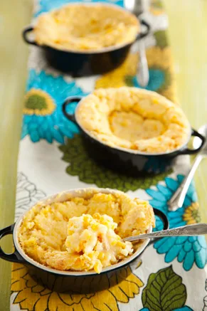 Paula Deen Southern corn casserole baked in black individual dishes with golden cheddar tops and a spoonful scooped out