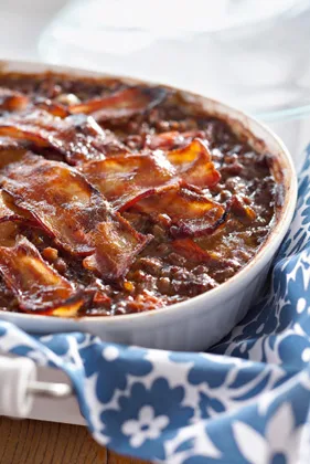 Paula Deen Southern ground beef and baked beans casserole topped with crisp bacon slices in a white baking dish