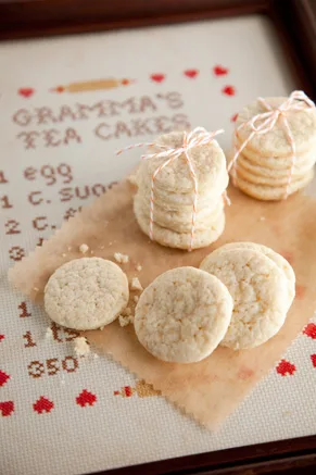 Paula Deen Southern Tea Cakes stacked and tied with baker's twine next to a cross-stitched Grandma's Tea Cakes sampler