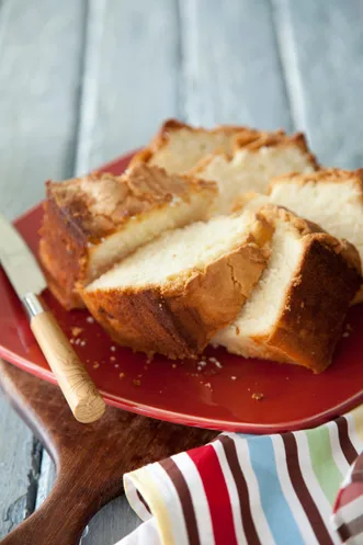 Sliced Paula Deen Southwest Georgia pound cake with a golden crust on a red plate next to a knife and a striped napkin