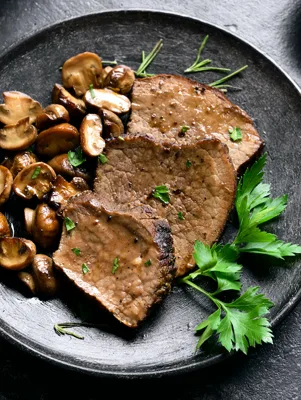 Paula Deen Steak Diane with sliced beef tenderloin, sauteed mushrooms and fresh parsley on a dark plate