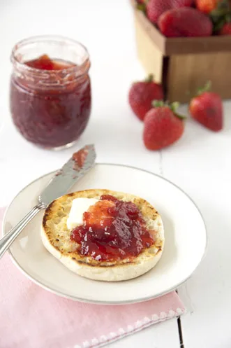 Paula Deen strawberry jam spooned over a toasted English muffin with butter next to a jar of jam and fresh strawberries