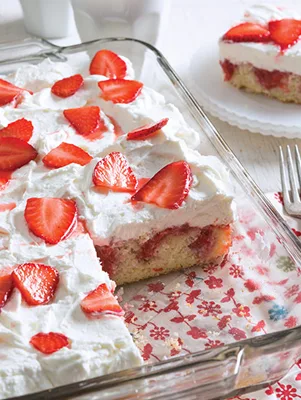 Paula Deen strawberry lemonade poke cake in a glass 13x9 dish topped with whipped cream and sliced strawberries, one slice cut out