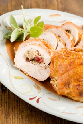 Paula Deen stuffed turkey breast sliced into pinwheels showing cornbread, pecan and cranberry stuffing on a decorative platter with fresh sage