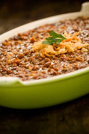 Paula Deen Sue and Gloria's baked beans with pineapple in a green baking dish topped with crispy fried onions and a parsley sprig
