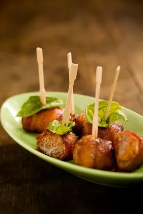 Paula Deen sweet chicken bacon wraps on wooden picks with fresh basil leaves in a green oval dish