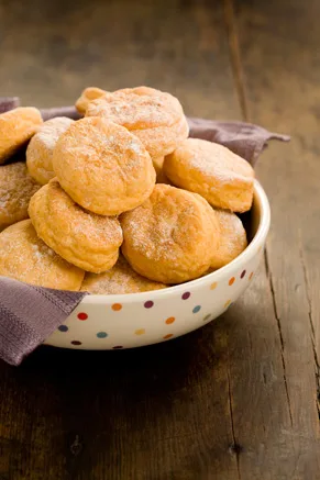Paula Deen sweet potato biscuits piled in a polka dot bowl lined with a gray cloth on a wooden table