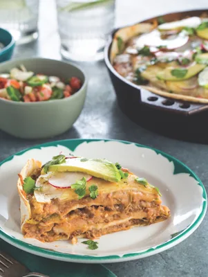 Slice of Paula Deen taco pie with layers of beef, beans and cheese topped with avocado, radish and cilantro on a green-rimmed plate