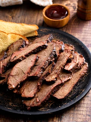 Paula Deen Texas brisket sliced on a black plate with toast and a small bowl of barbecue sauce