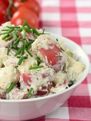 Paula Deen Texas country Southern potato salad with red potatoes, chopped chives and creamy dressing in a white bowl on a red gingham cloth