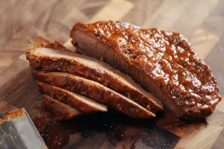 Sliced Paula Deen Texas oven-roasted beef brisket with a dark glossy crust on a wooden cutting board