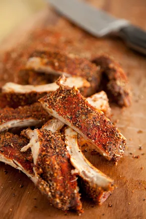 Paula Deen Texas pork ribs cut into pieces on a wooden board, coated in a dark paprika and black pepper dry rub