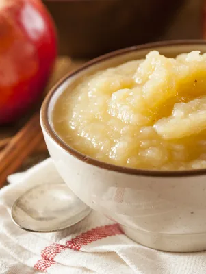 Paula Deen The Best Homemade Applesauce, thick chunky applesauce in a cream bowl next to a red apple and cinnamon sticks