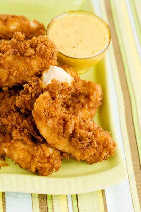 Paula Deen The Lady and Sons chicken fingers stacked on a green plate with a small bowl of honey mustard dipping sauce