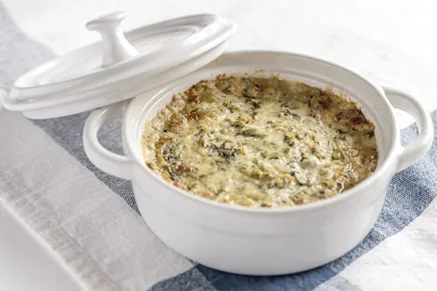 Paula Deen three cheese hot artichoke dip baked golden and bubbly in a white round baking dish with a lid