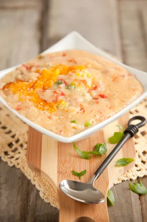 Paula Deen tomato grits baked casserole with melted cheddar, diced tomatoes and green onions in a white square dish