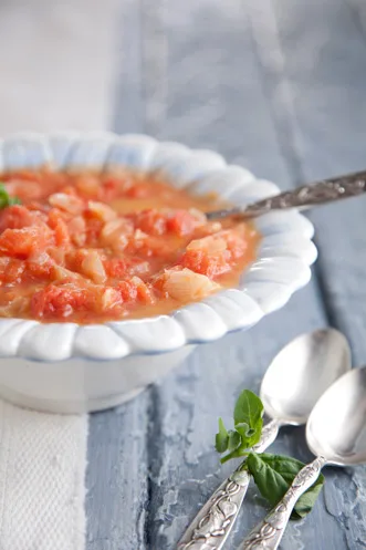 Paula Deen tomato soup, a chunky fresh tomato soup in a white scalloped bowl with a spoon and fresh basil beside it