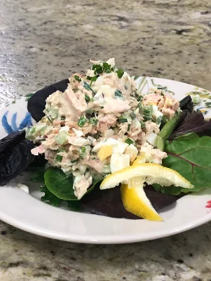 Paula Deen tuna salad with chopped egg and chives served on mixed greens with a lemon wedge on a white plate