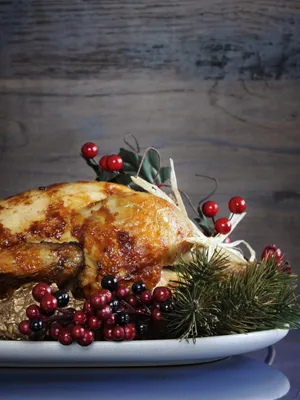 Paula Deen turducken golden roasted whole bird on a white platter with red berries and evergreen garnish