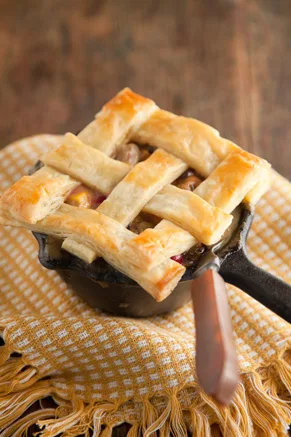 Paula Deen turkey pot pie in a small cast iron skillet topped with a golden puff pastry lattice on a yellow checked towel