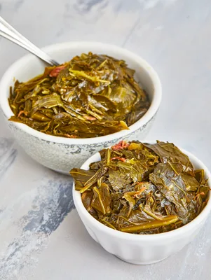 Two bowls of Paula Deen turnip & mustard greens, tender and glossy, served with a spoon on a light surface