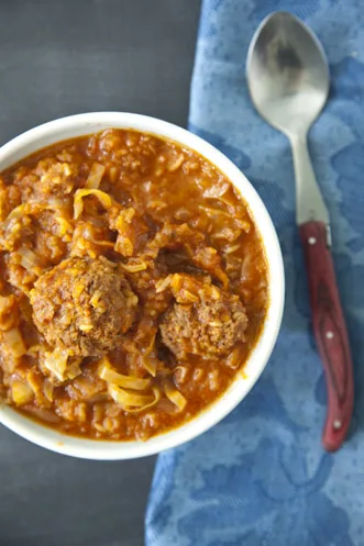 Paula Deen un-stuffed cabbage soup with meatballs in a white bowl with cabbage ribbons in tomato broth