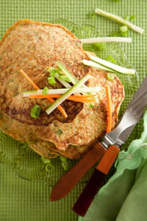 Paula Deen vegetable pancakes stacked on a glass plate topped with sliced green onions and carrot and zucchini matchsticks