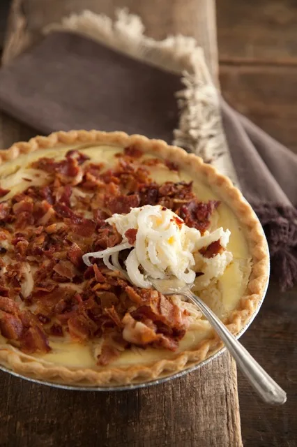 Paula Deen Vidalia onion pie topped with crumbled bacon in a golden crust with a forkful of creamy onions lifted from the pie