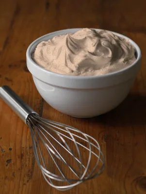Paula Deen whipped pumpkin cream piled in a white bowl with a whisk resting on a wooden table